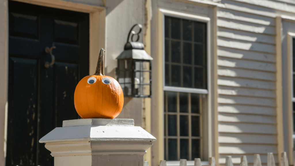 A bright orange pumpkin on a wooden front porch decorated for Halloween.