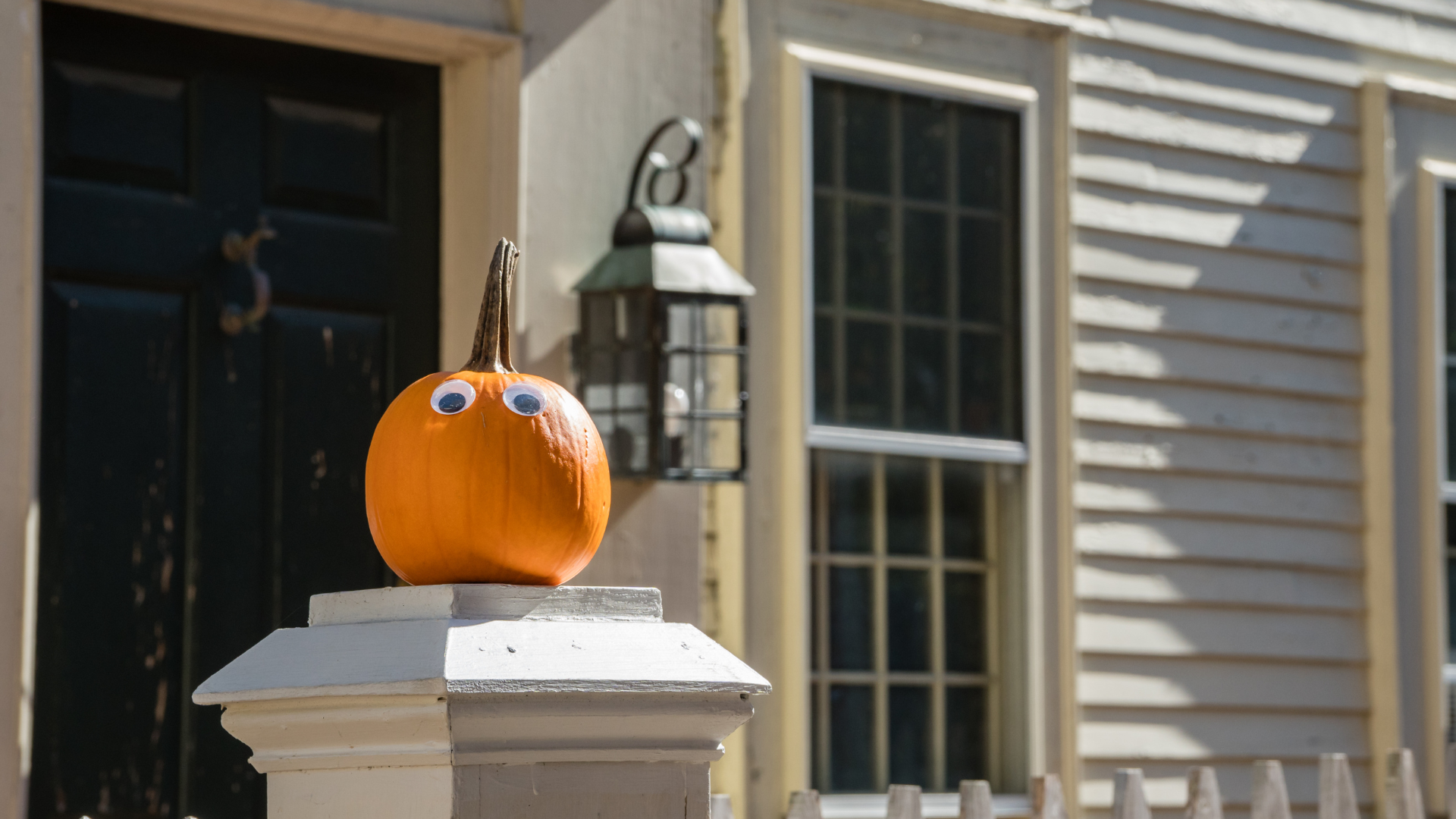 A bright orange pumpkin on a wooden front porch decorated for Halloween.